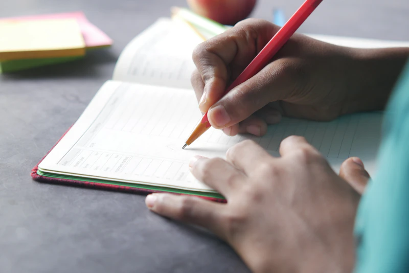Des mains qui écrivent au crayon dans un cahier d'école